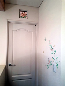 ドアの上にはバラのステンドグラス、壁にはステンシルで描いたバラや蝶