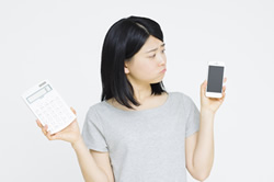 電卓とスマホを持っている女性の画像